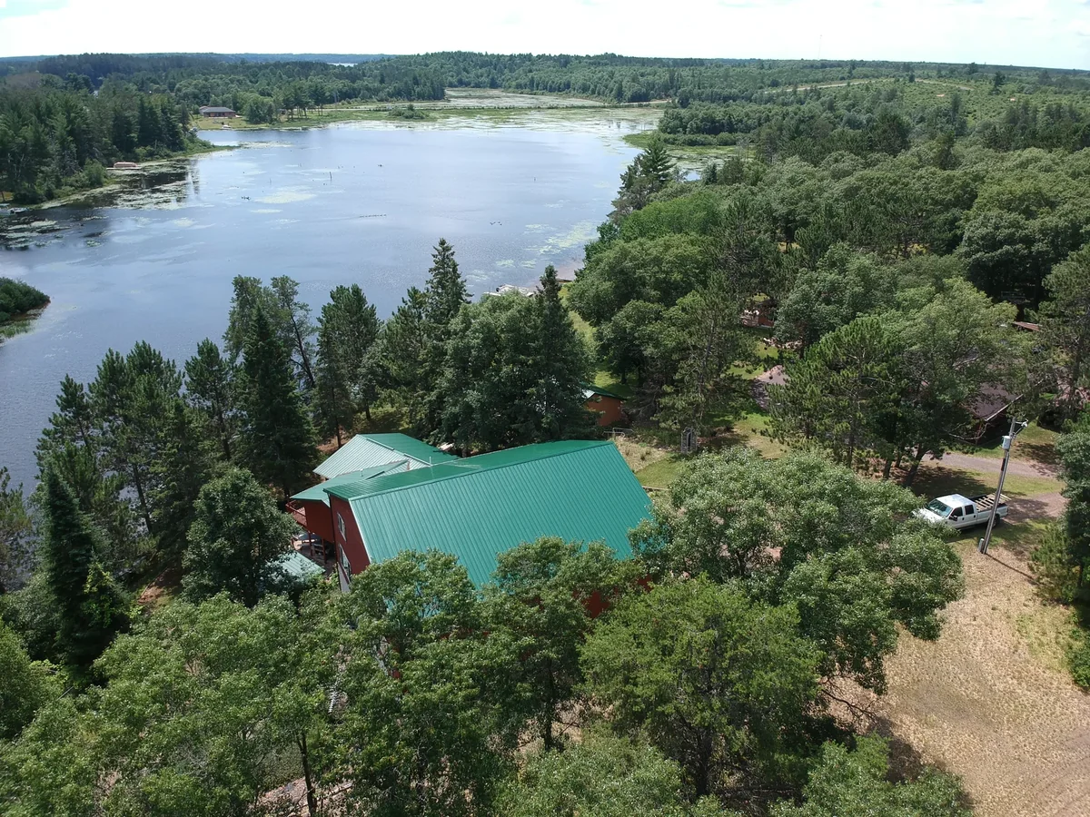 Aerial view over a river of a red home with a green metal roof set among trees near Grantsburg, WI
