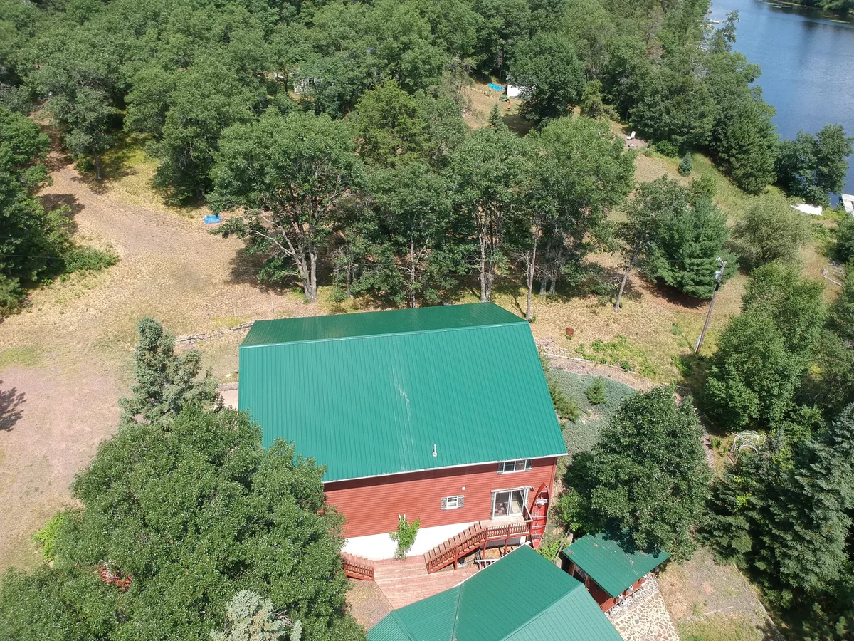 Angled drone shot of the green standing seam roof above the red two-story home and surrounding woods