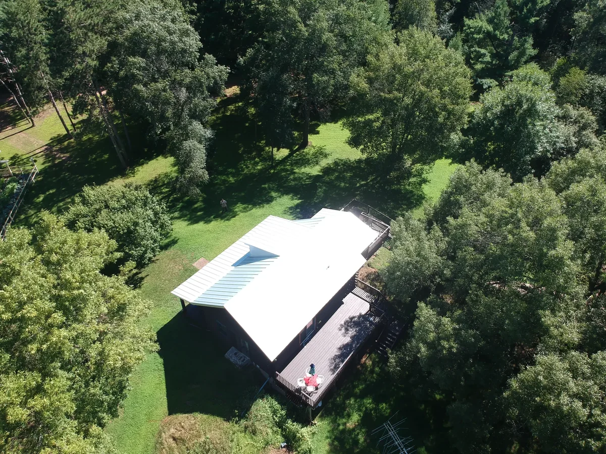 Overhead aerial of a silver galvalume standing seam roof on a home set in a wooded clearing in Harris, MN.