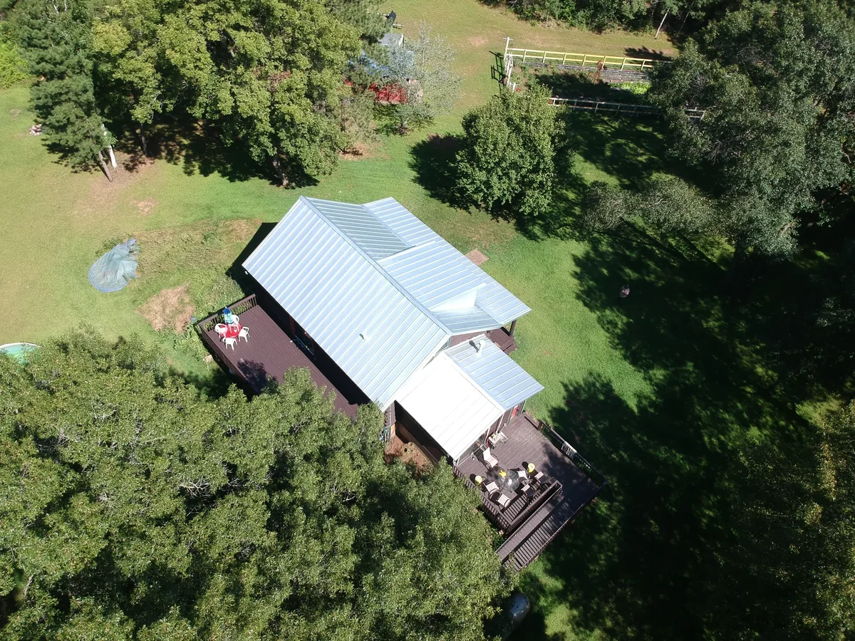 Angled view of the bright metal roof joining a darker addition with the yard and trees around it.