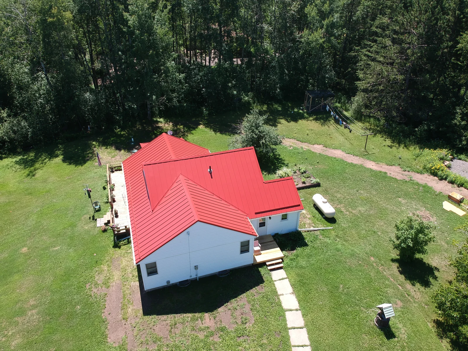 Aerial view of a cabin near Hayward, WI with a bright red metal roof set in a grassy clearing