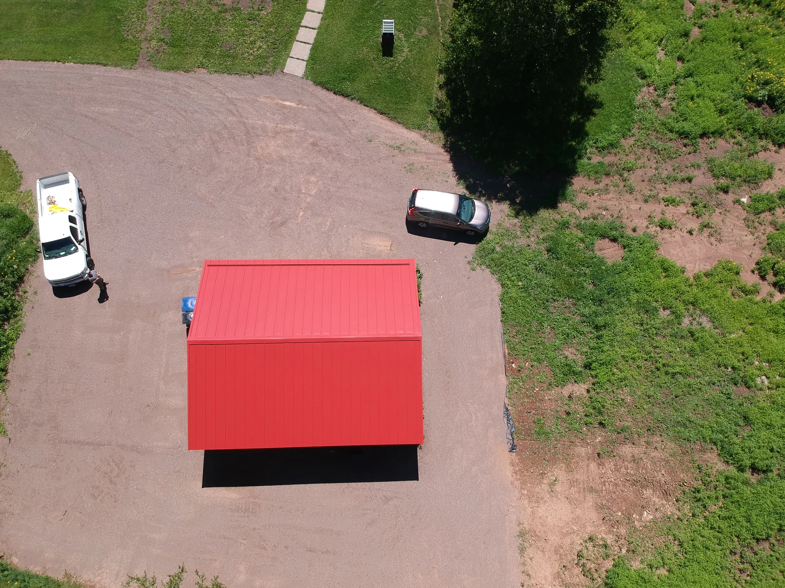 Close aerial of the red metal roof on the outbuilding with vehicles parked on the drive