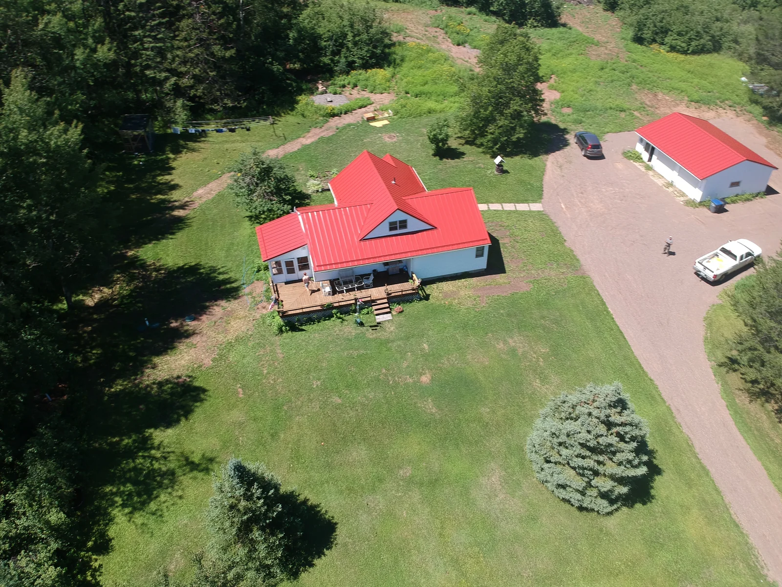 Angled drone shot of the red-roofed home framed by the encircling treeline