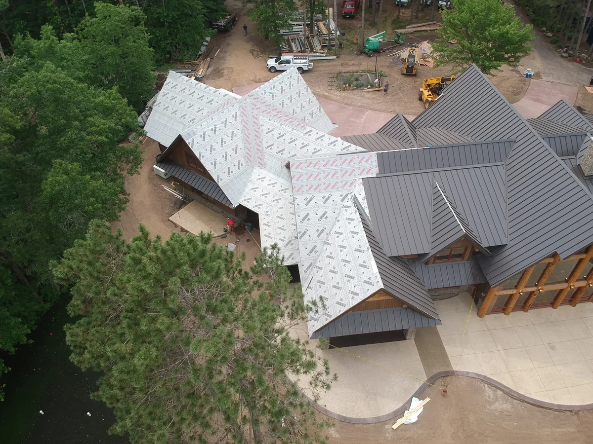 Elevated view of the sprawling roof showing finished standing seam panels beside exposed underlayment.
