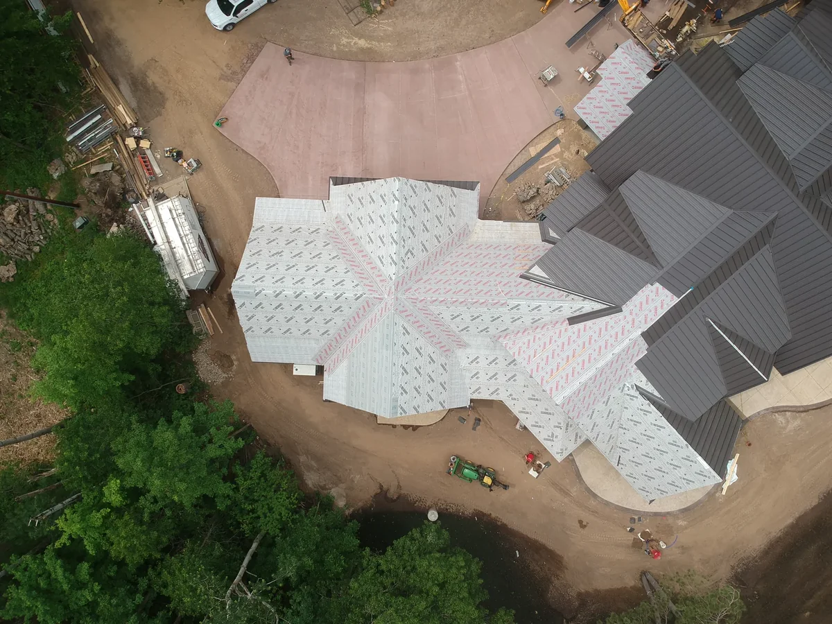 Drone shot of the complex roof layout with multiple gables and a wooded backdrop.