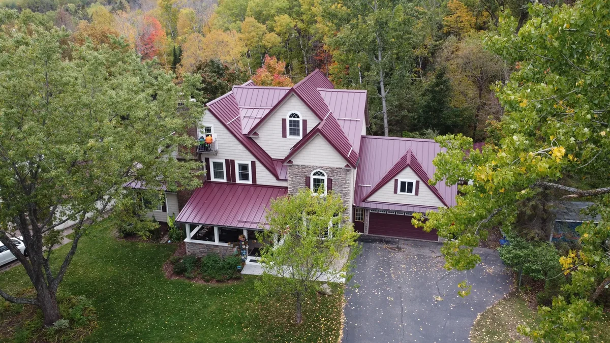 Drone shot of the burgundy standing seam roof among colorful autumn trees