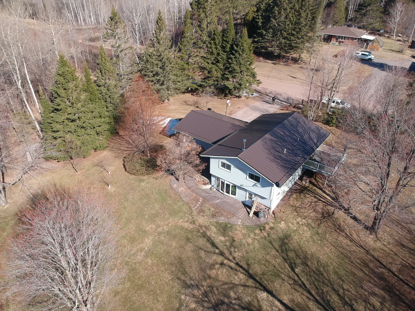 Aerial view of a brown metal roof on a ranch home near Hibbing, MN, set on a wooded lot with bare early-spring trees.