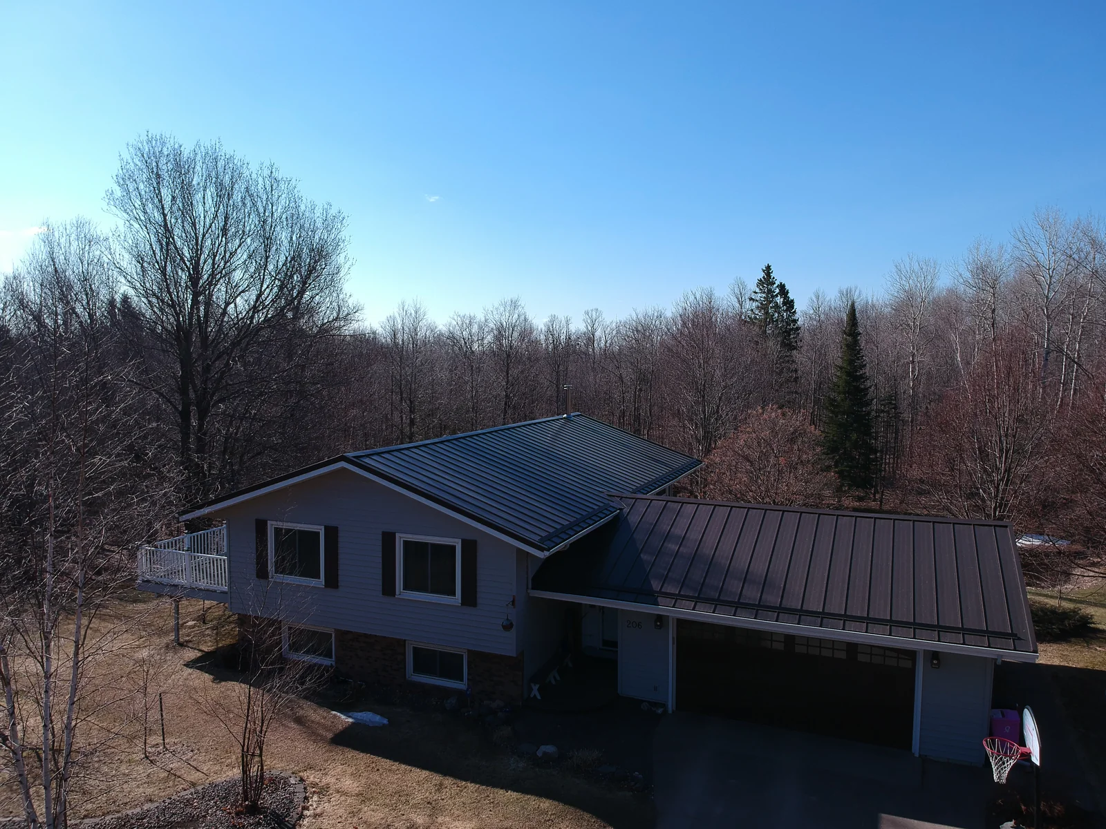 Split-level house with a dark bronze metal roof and matching gutters beside a forest edge.