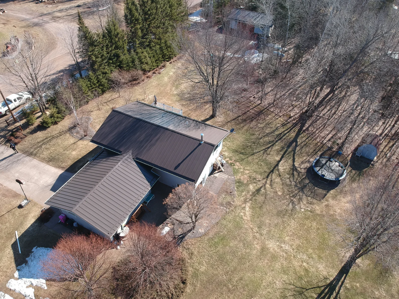 Drone angle of the bronze-roofed home with a detached garage among leafless trees.