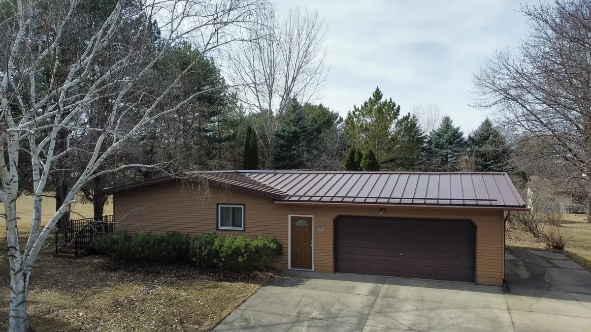 Front aerial view of a tan brick ranch home with a bronze standing seam metal roof in Hibbing, MN