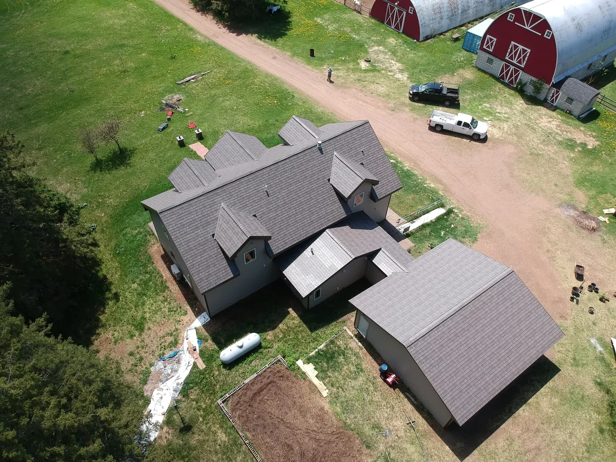Distant aerial showing the metal-roofed home with a red barn outbuilding at the property edge.