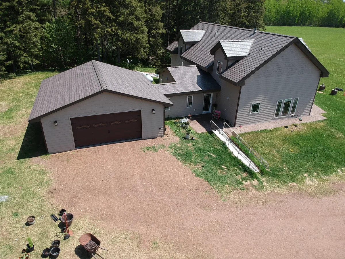 Low aerial of the garage and driveway beneath the sweeping metal shingle roofline.