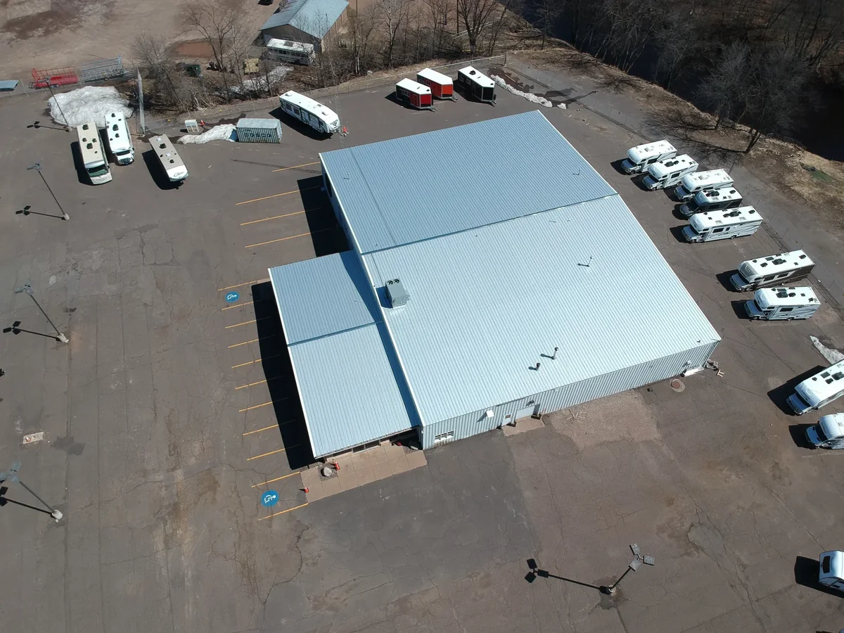 Angled aerial of the white roof with the parking lot and surrounding trees