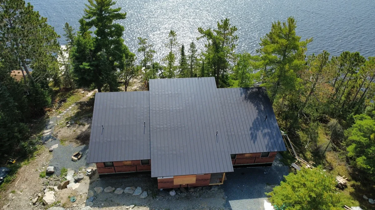 Aerial view of a lakeside home with a dark gray metal roof tucked into the pines in International Falls, MN