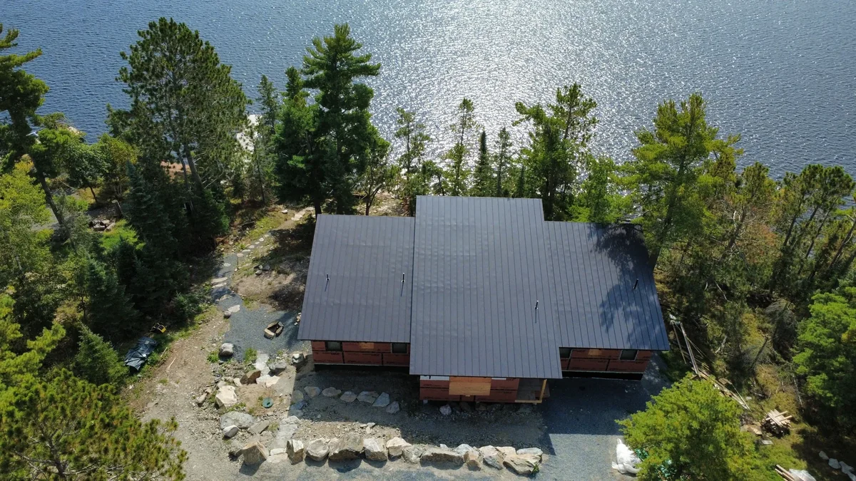 Drone shot of the gray-roofed home overlooking the water through the trees