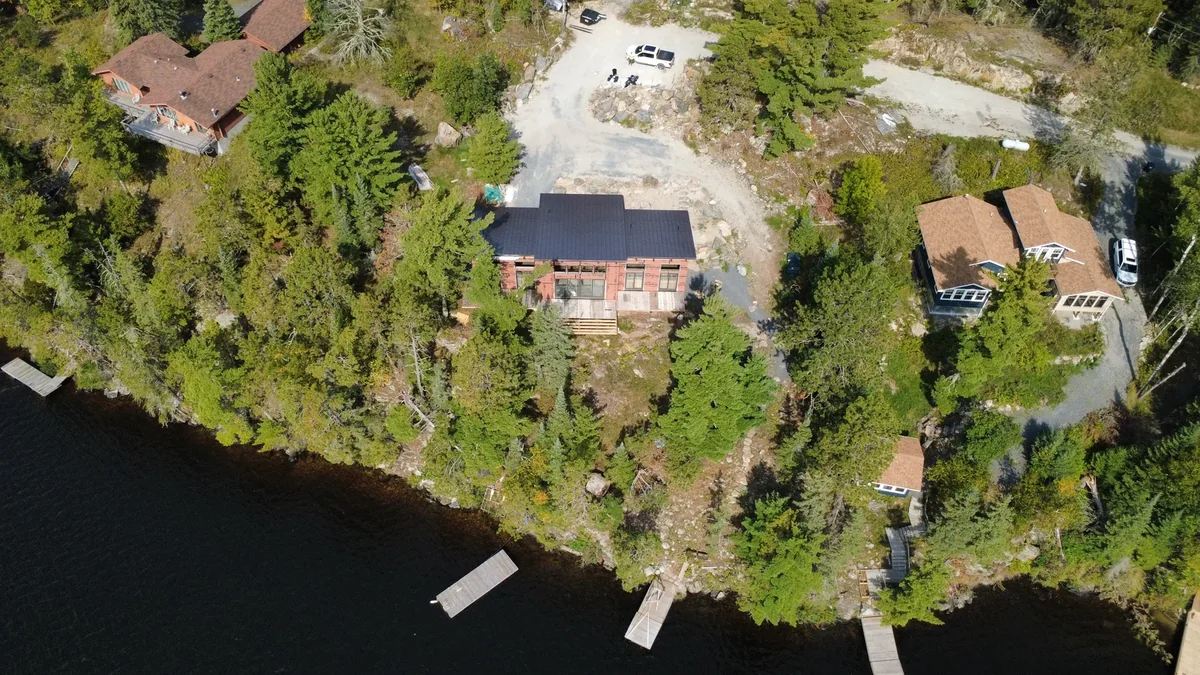 High view of the property with the metal-roofed home and dock along the shoreline