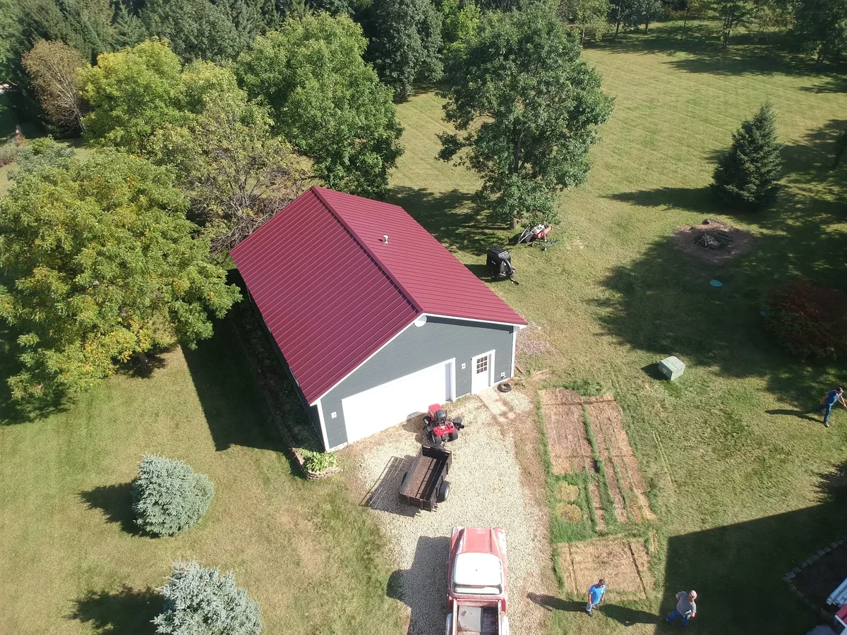 Aerial view of a deep red metal roof on a home near Inver Grove Heights, MN, surrounded by green lawn and mature trees.