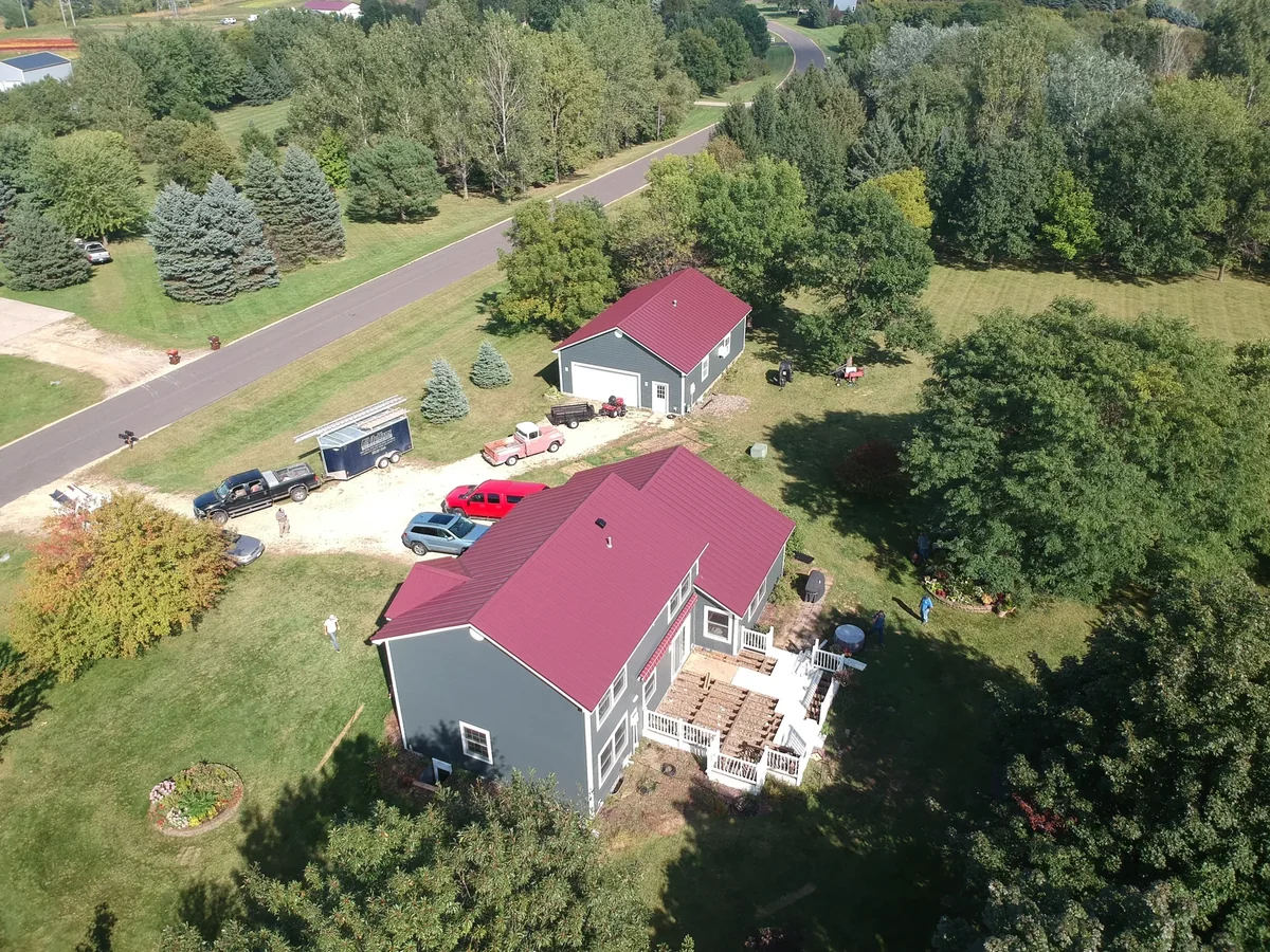 Drone view of the red-roofed home and outbuilding with a quiet country road beyond.
