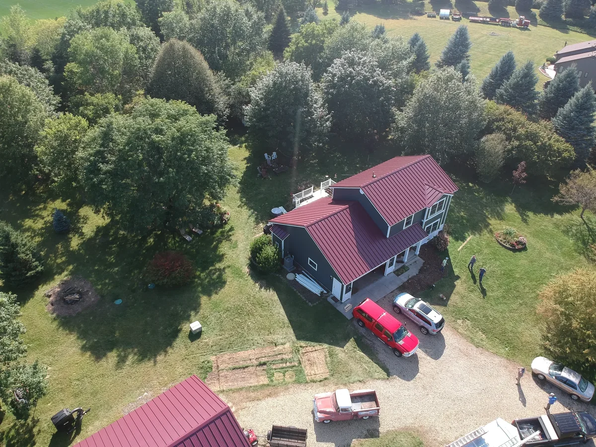 Overhead angle of the red metal roof with vehicles and garden beds in the yard below.