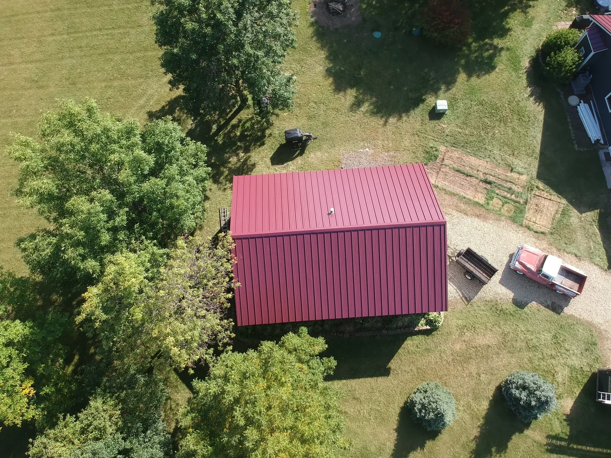 Top-down view of a red-roofed pole building set among trees on the property.