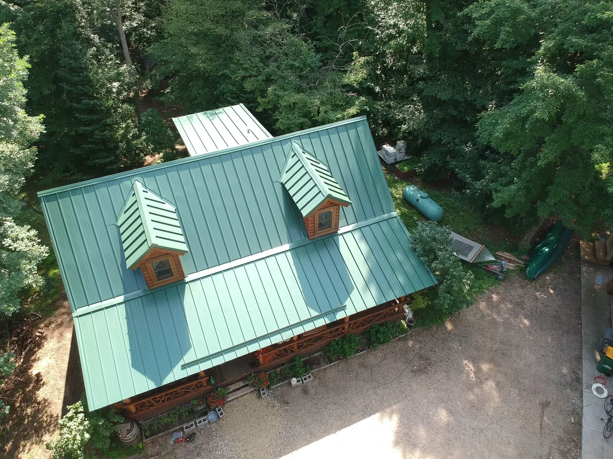 Overhead aerial of a green standing seam metal roof with dormers and a cupola on a wooded lot in Isanti, MN.
