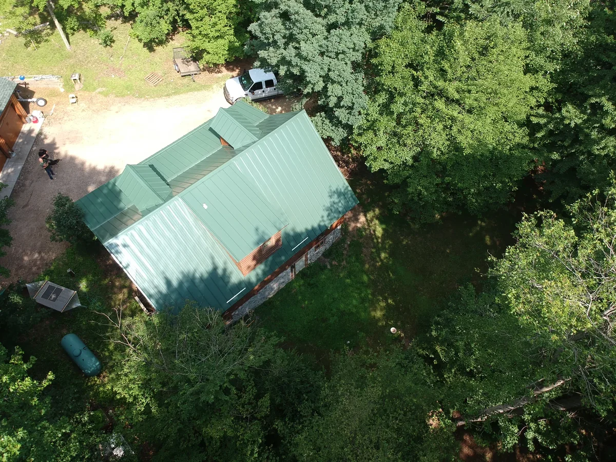 Green metal roof seen from above with vehicles parked in the shaded yard.