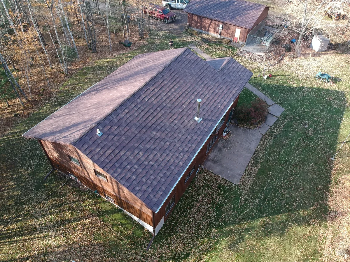 Aerial view of a single-story home with a brown metal shingle roof set in a wooded lot in Isle, MN.
