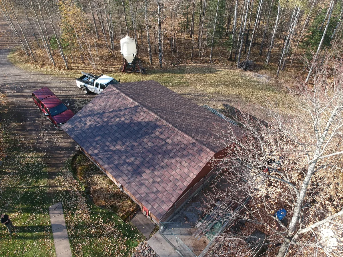 Drone shot of the long metal shingle roof with vehicles parked in the gravel drive.