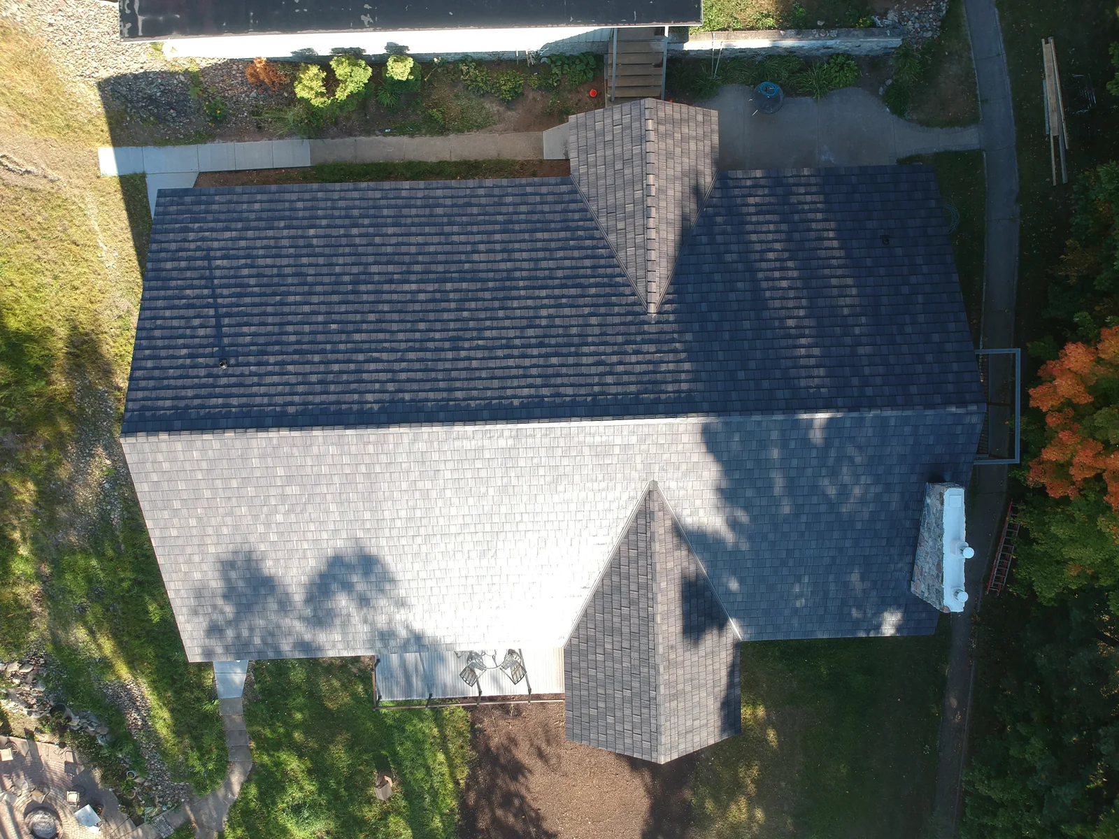 Aerial view of a gray metal shingle roof on a lakeside home near Lake Vermilion, MN, with a stone chimney and wooded shoreline.