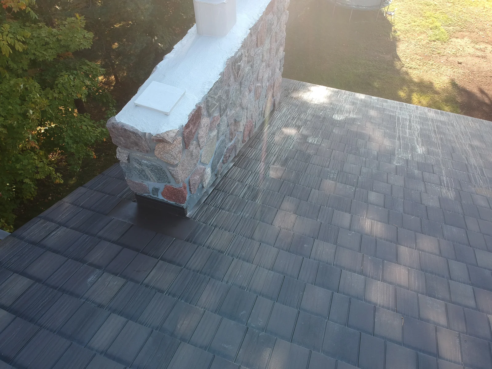 Close overhead of the textured gray metal shingles meeting a tall stone chimney.