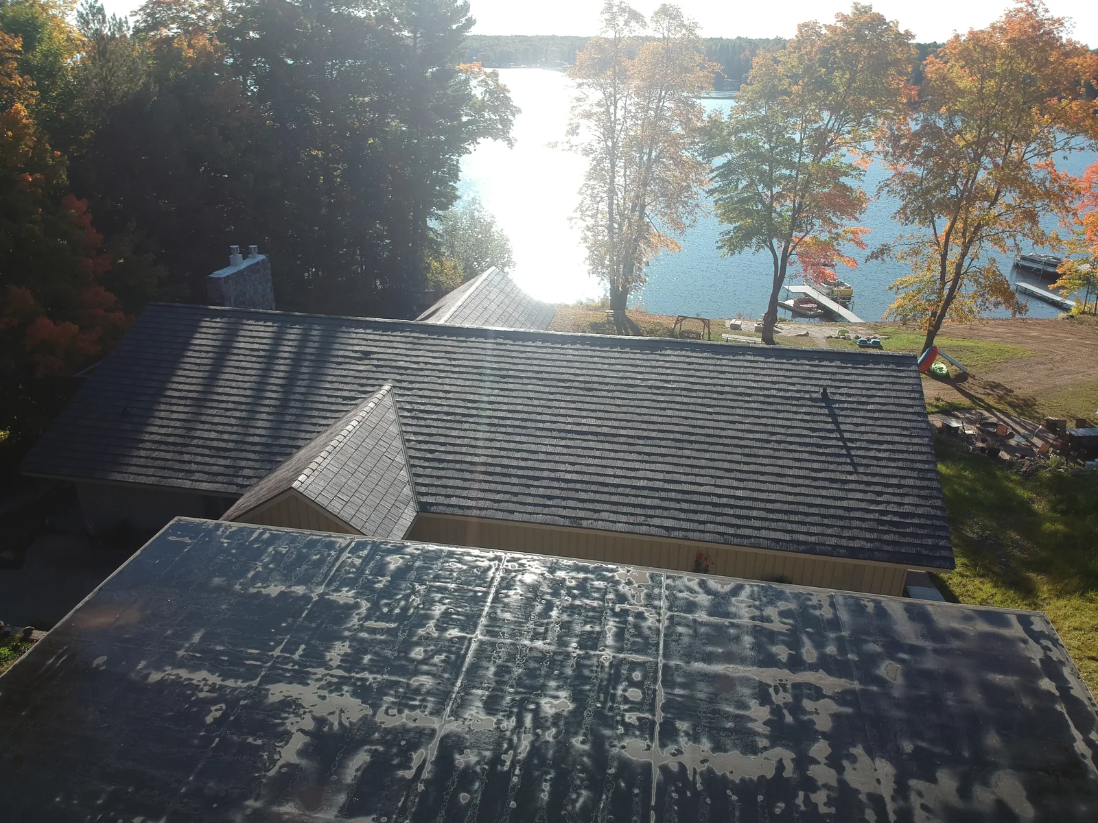 Metal shingle roofline framing a view down to the lake through the autumn trees.