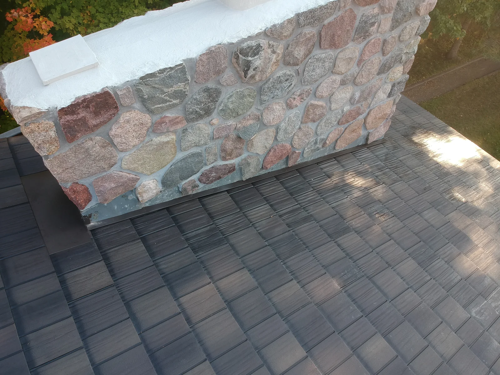 Detail of the stone chimney rising from the gray metal shingle roof slope.