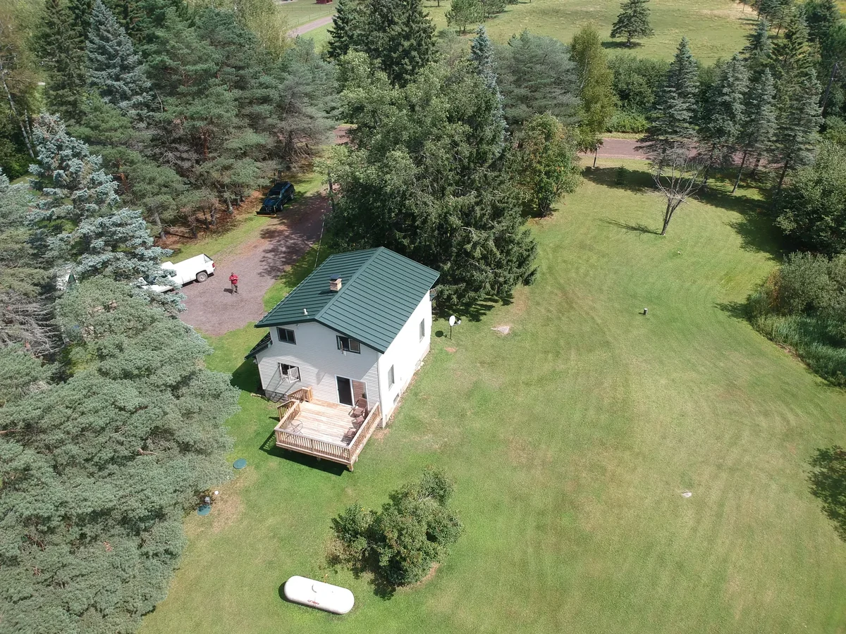 The blue metal roof and white home framed by towering pines across the green lawn.