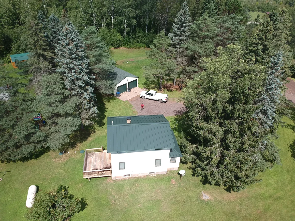 Side view of the white home showing the blue metal roof above the rear deck.