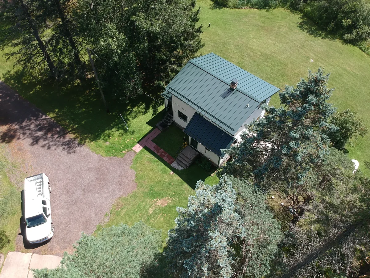 Angled aerial of the blue metal roof with the curving driveway and a parked van.