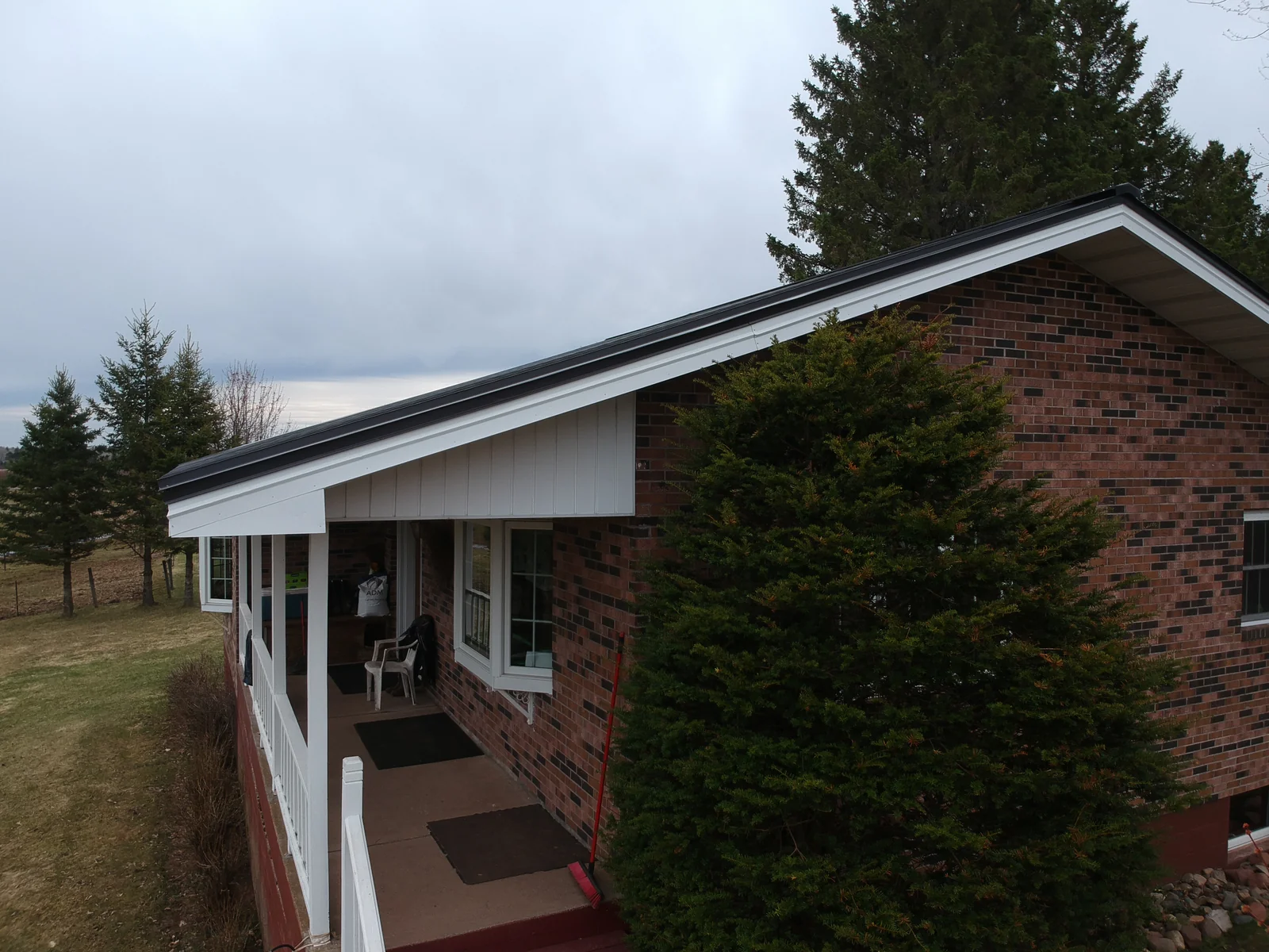 Angled aerial of the gray metal roof above the brick walls framed by evergreens