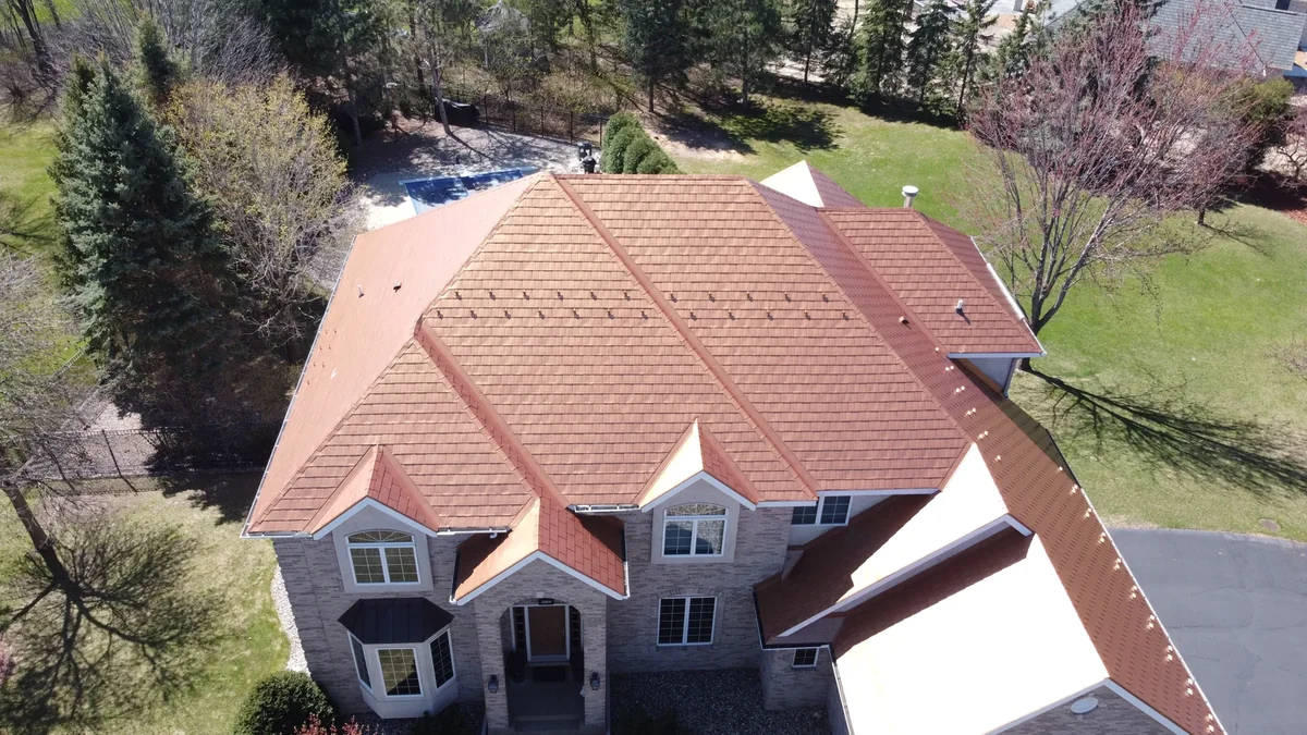 Aerial view of a terracotta stone-coated metal tile roof on a large stucco home in Minneapolis, MN, with a manicured lawn.
