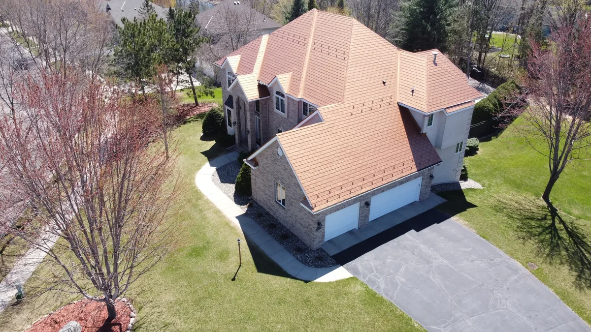Side angle showing the stone-coated metal roof wrapping the gables and the driveway below.