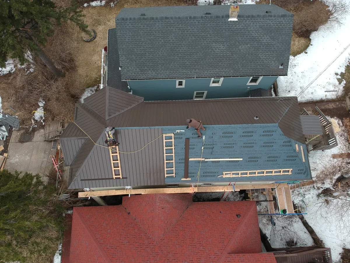 Overhead view of the bronze metal roof beside the home's gray shingled section and a red neighboring roof