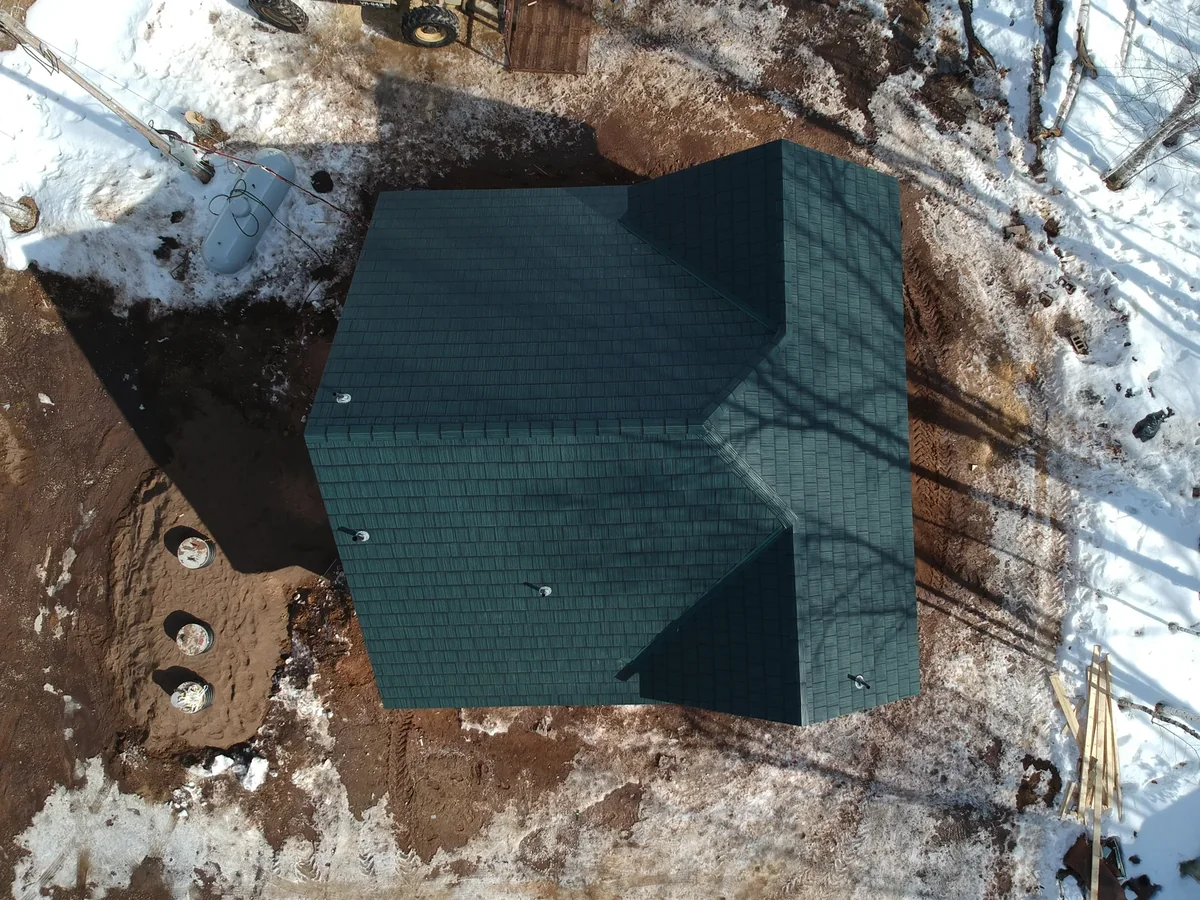 Overhead view of the multi-gabled green metal shingle roof and the muddy work site