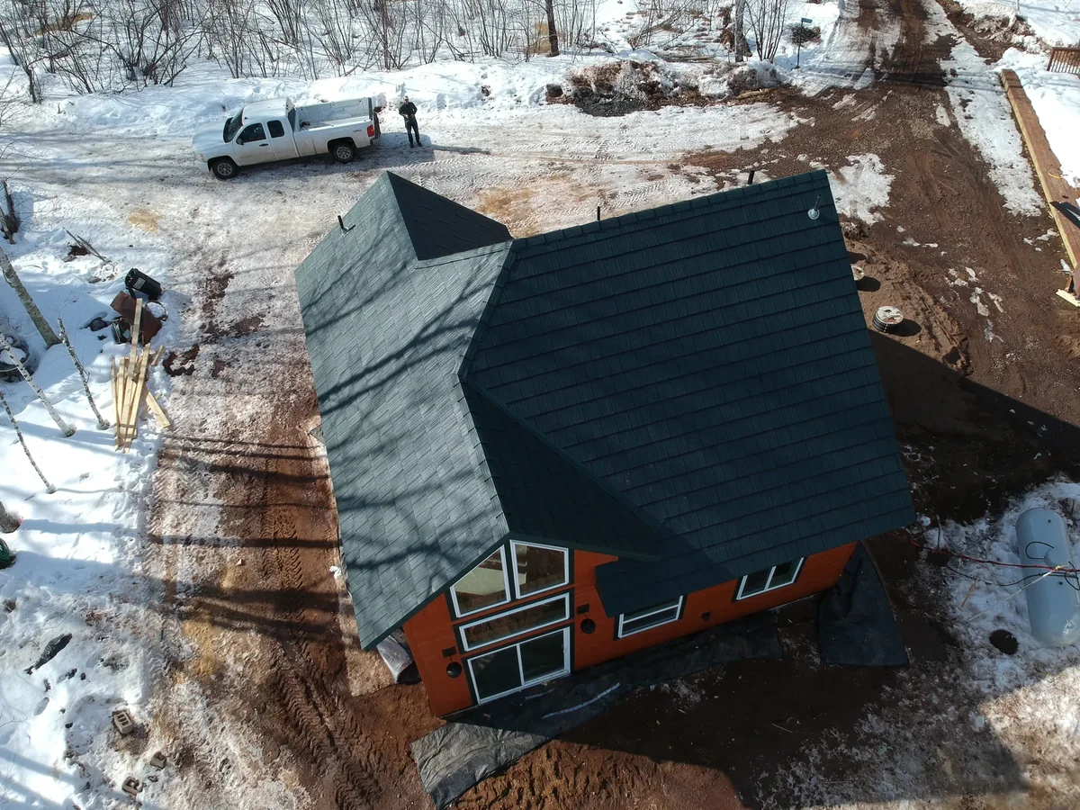 Angled aerial of the green metal shingle roof with construction equipment parked nearby