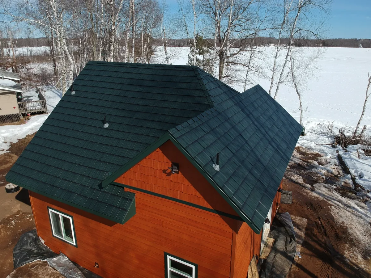 Close aerial of the green metal shingle roof slopes meeting at the ridge over the orange walls