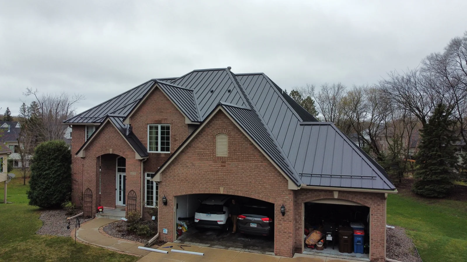 Front aerial view of a large brick home with a dark gray standing seam metal roof in Owatonna, MN.