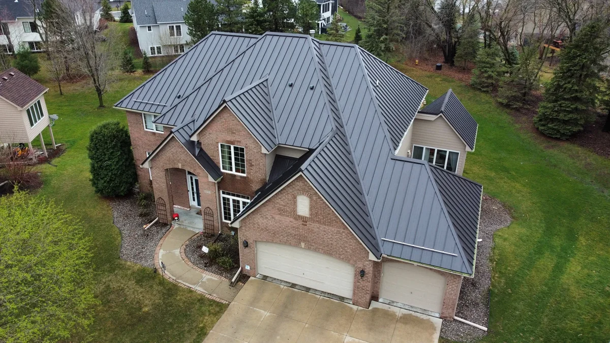 Angled drone shot of the brick home's gray metal roof and attached three-car garage.