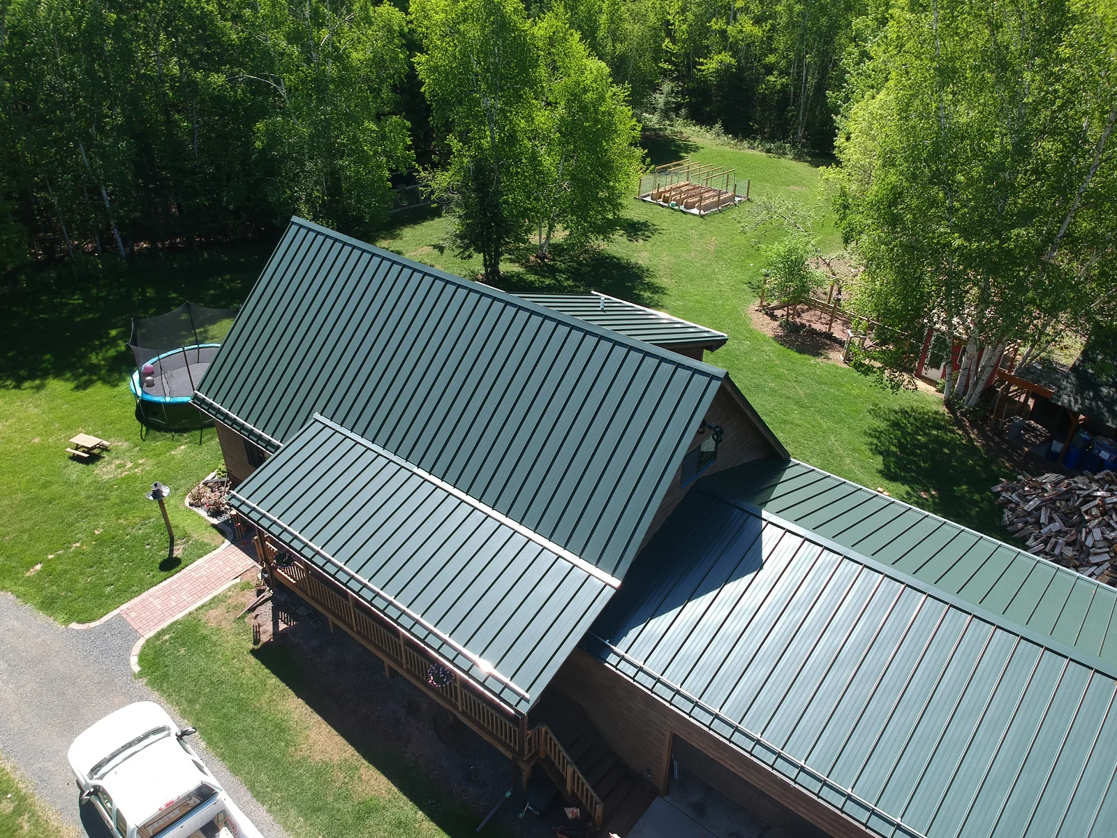 Aerial view of a country home with a green standing seam metal roof and detached garage near Poplar, WI