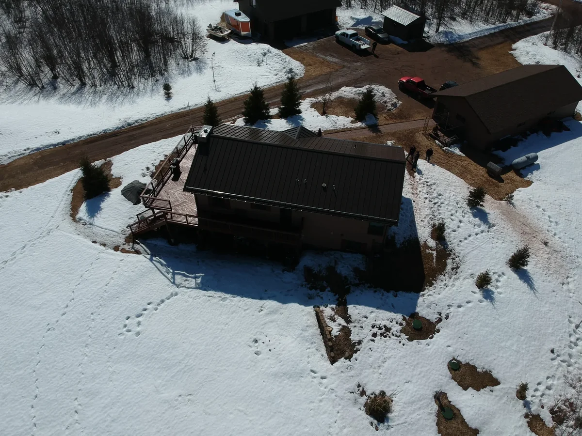 Aerial view of a bronze standing seam metal roof on a rural building near Proctor, MN, surrounded by snow-covered ground.