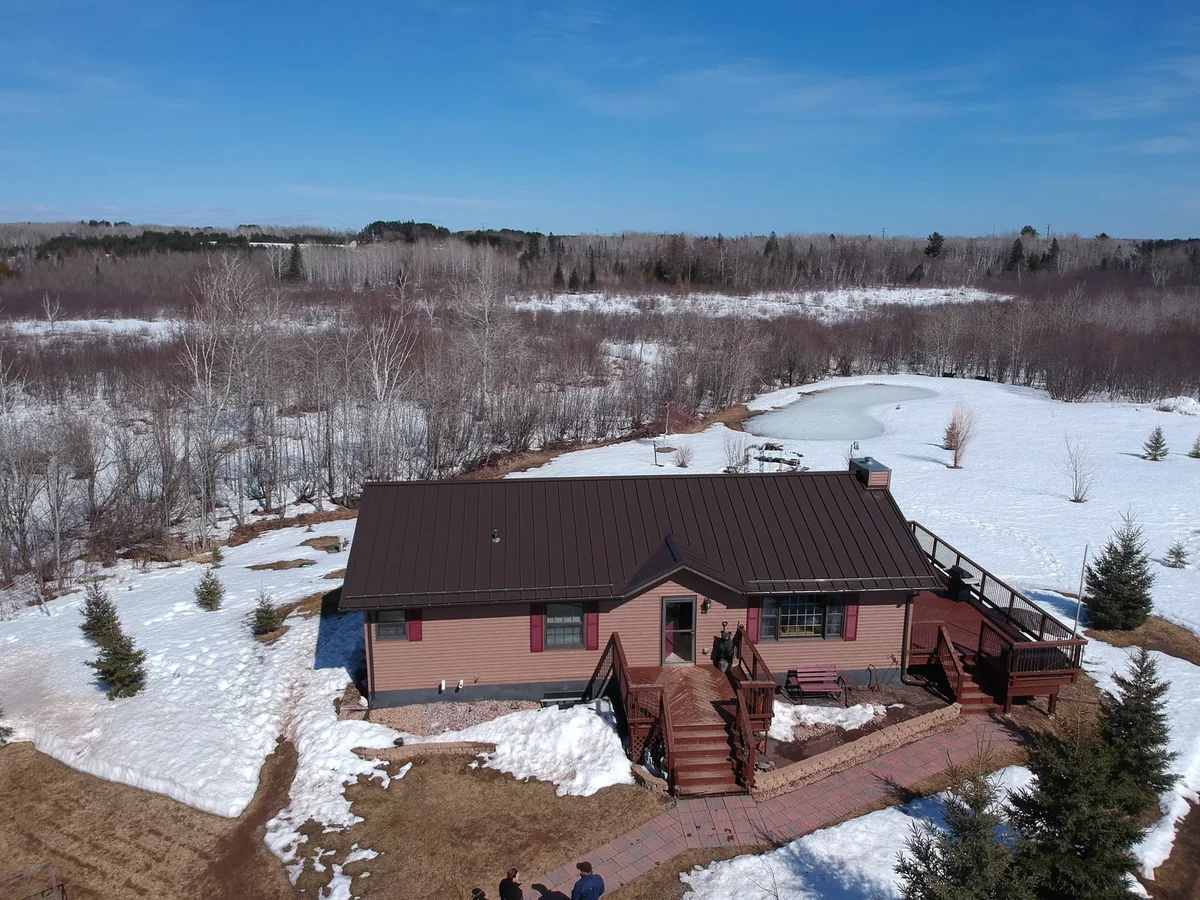 Bronze-roofed home with a wraparound deck overlooking an open snow-covered field.