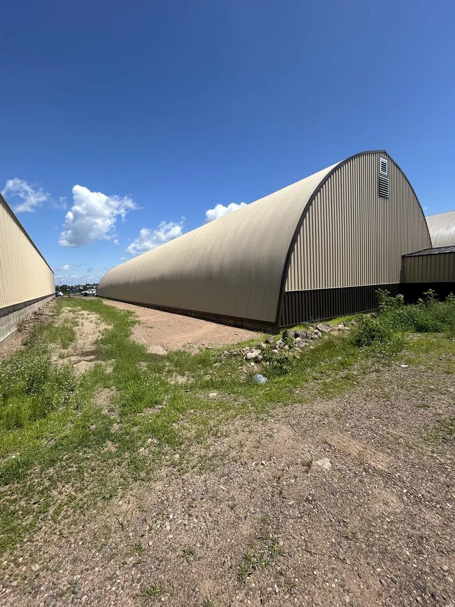 Ground-level view of a long arched metal commercial building with a curved standing seam roof in Rice Lake, WI
