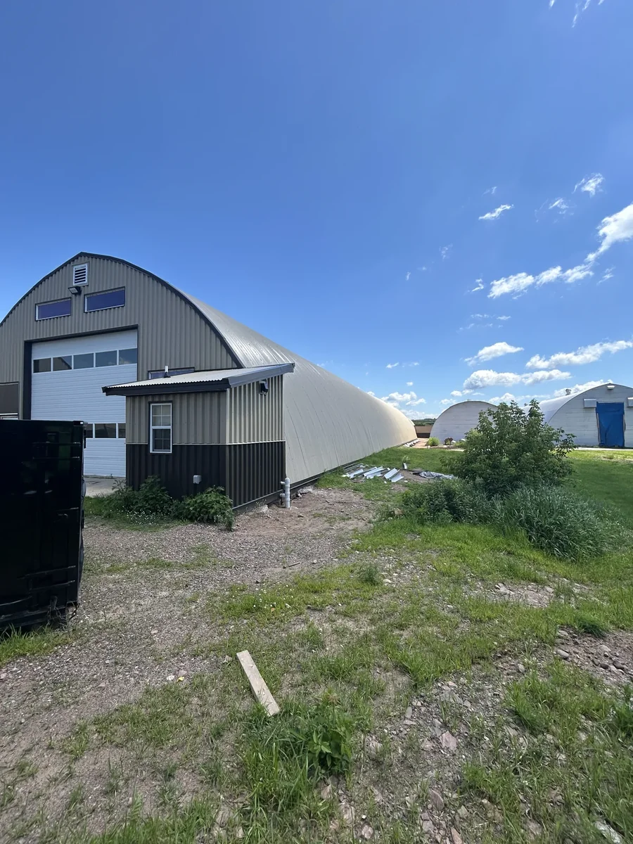 An adjacent metal structure beside the arched building under a blue summer sky