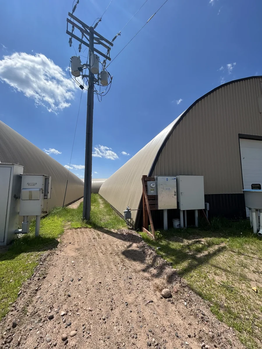 A gravel path running between two curved metal buildings past a power pole